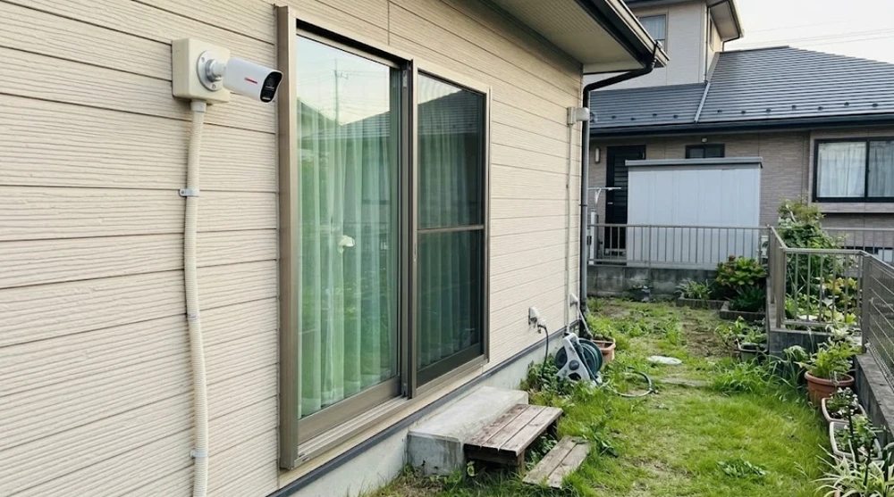 一戸建ての庭側の掃き出し窓のすぐ上に、目立つ白い防犯カメラを設置した様子