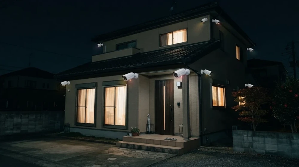 夜の一戸建て。玄関の両側と家の角や2階の軒下に、目立つ白い防犯カメラがいくつも付いている